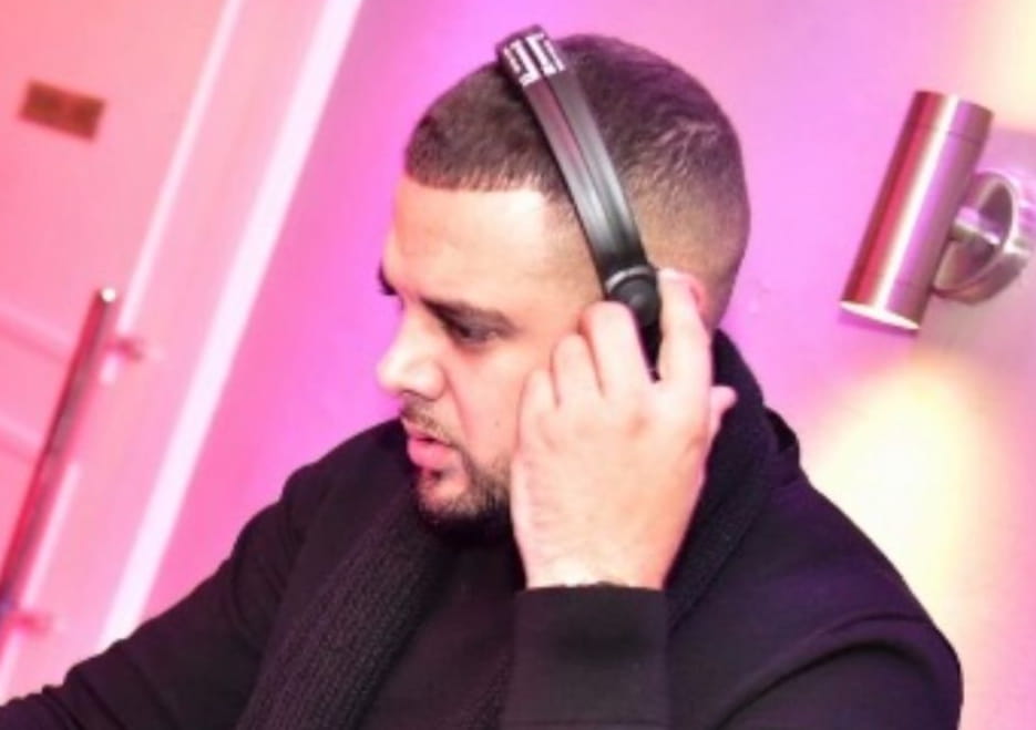 A man wearing headphones is mixing music in a vibrant setting with pink lighting.