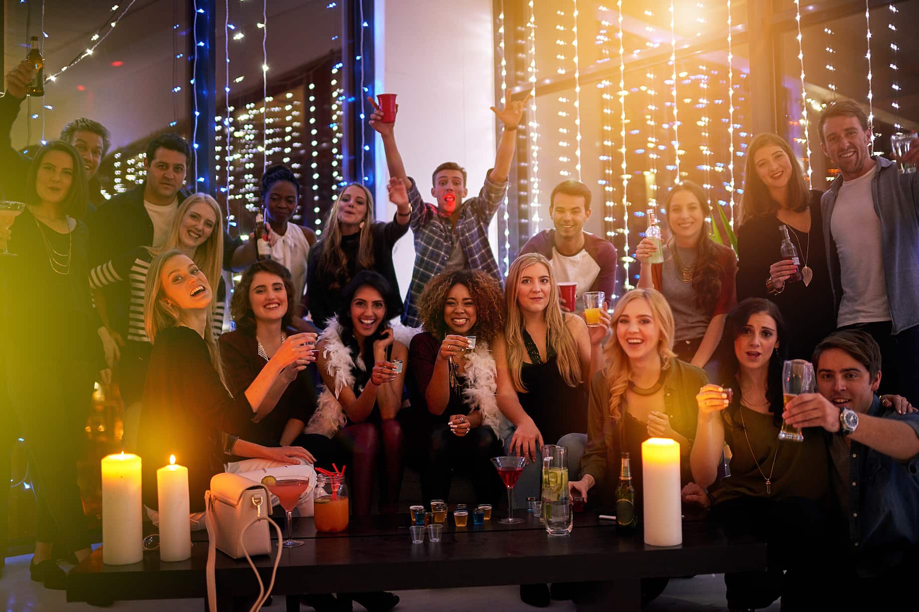 A group of young adults enjoying a party among festive decorations with drinks in hand.
