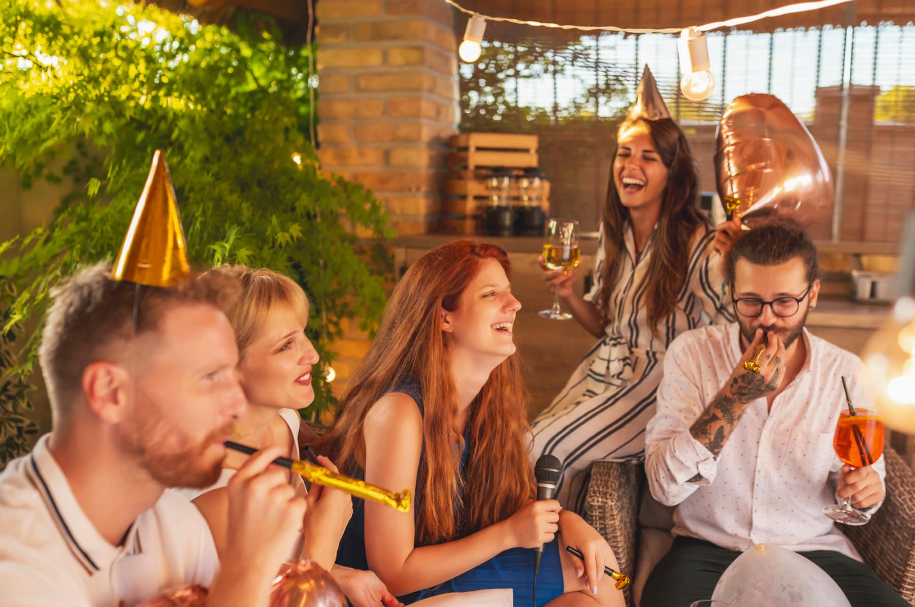 A group of five people celebrating together, wearing party hats and enjoying drinks, with laughter and a festive atmosphere.