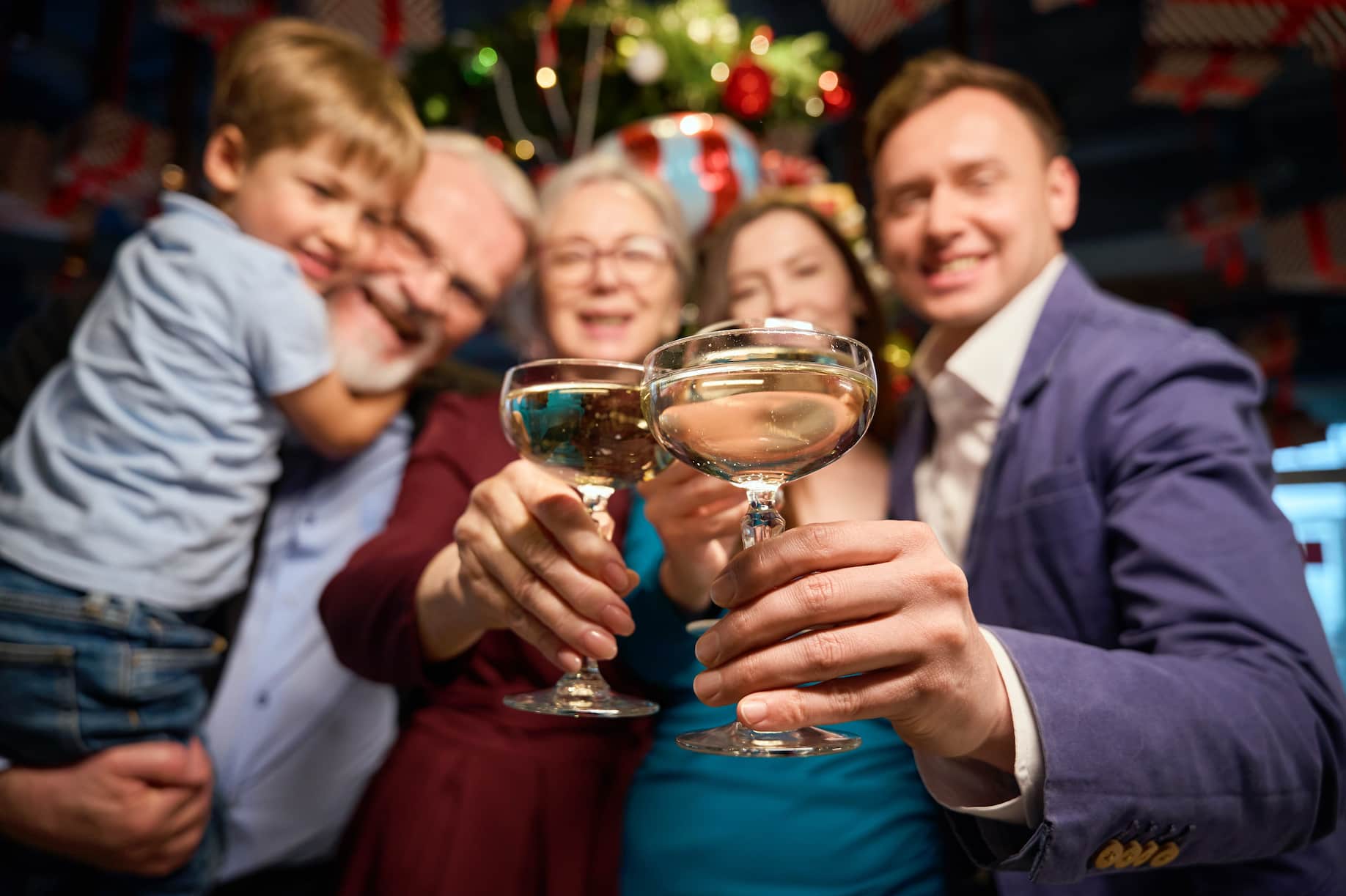 A group of five people, including a child, are smiling and raising glasses in a celebratory setting decorated with holiday ornaments.
