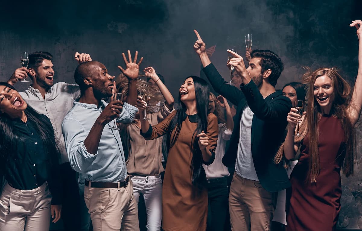 A group of people joyfully celebrating with drinks, dancing, and laughing in a festive atmosphere.