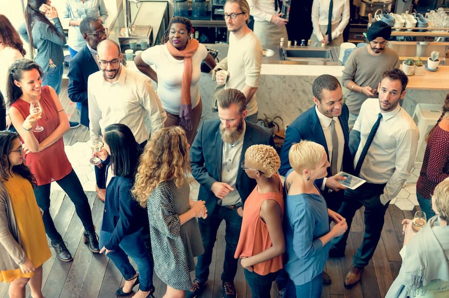 A diverse group of people socializing at a modern event, some holding drinks and engaging in conversation.