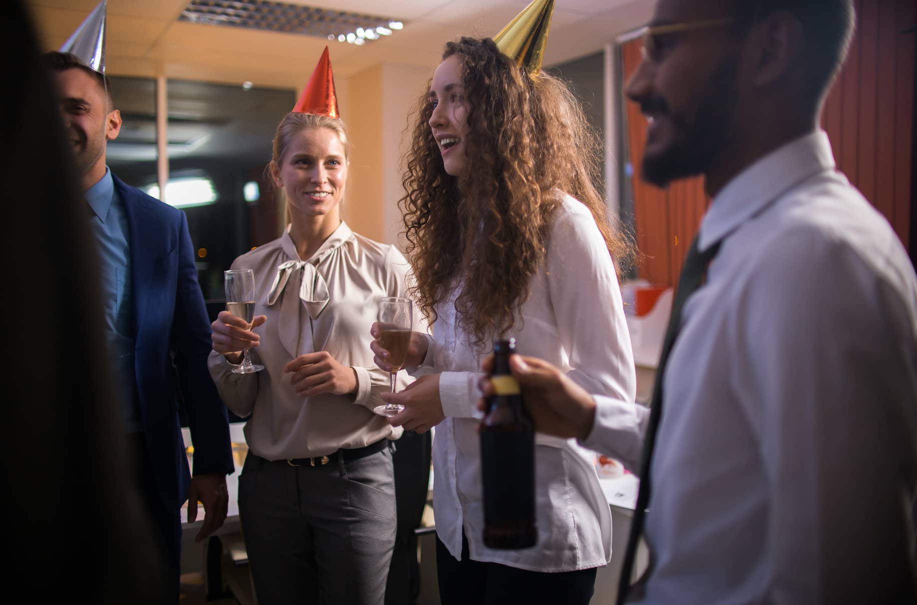 A group of people celebrating with party hats and drinks in an office setting.