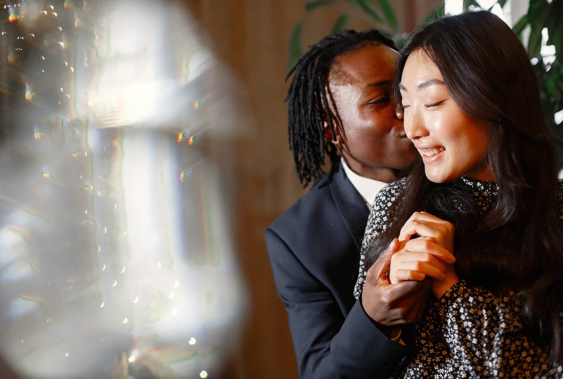 A couple is smiling and embracing each other in a cozy setting, with one partner leaning in for a kiss.