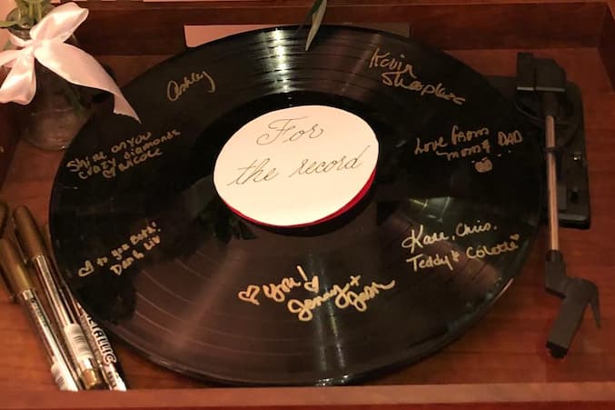A signed vinyl record with a white label reading 'For the record,' surrounded by decorative pens and a small bouquet.