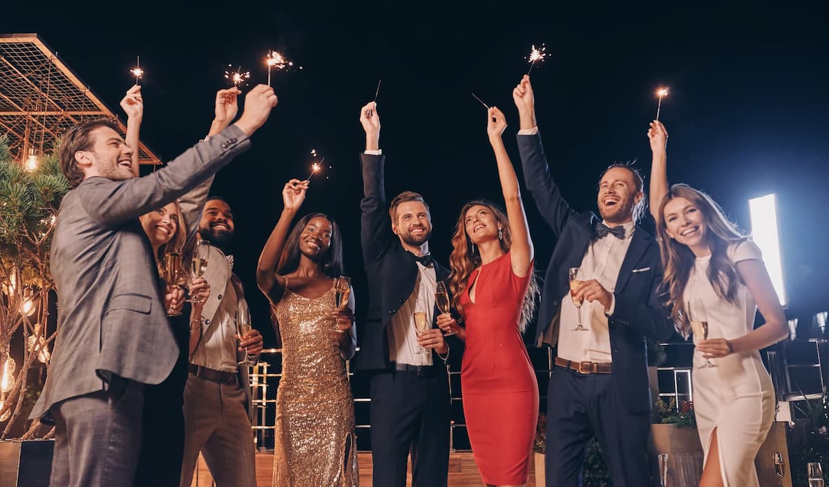 A group of people joyfully celebrating at night, holding sparklers and champagne glasses, wearing formal attire.